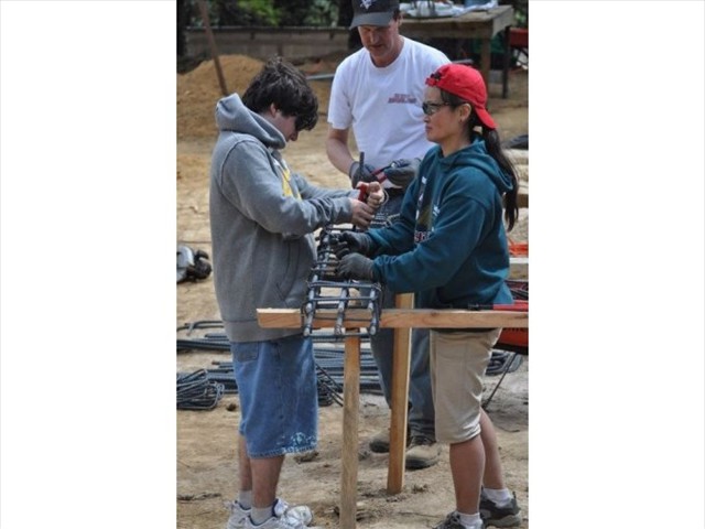 Edward, Jess, and Lars making a assemble line creating the rebar with pliers and wire in order to make the posts to hold the cement for the children's hospice foundation, one by one.